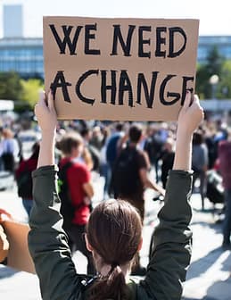 Person holding We Need A Change sign